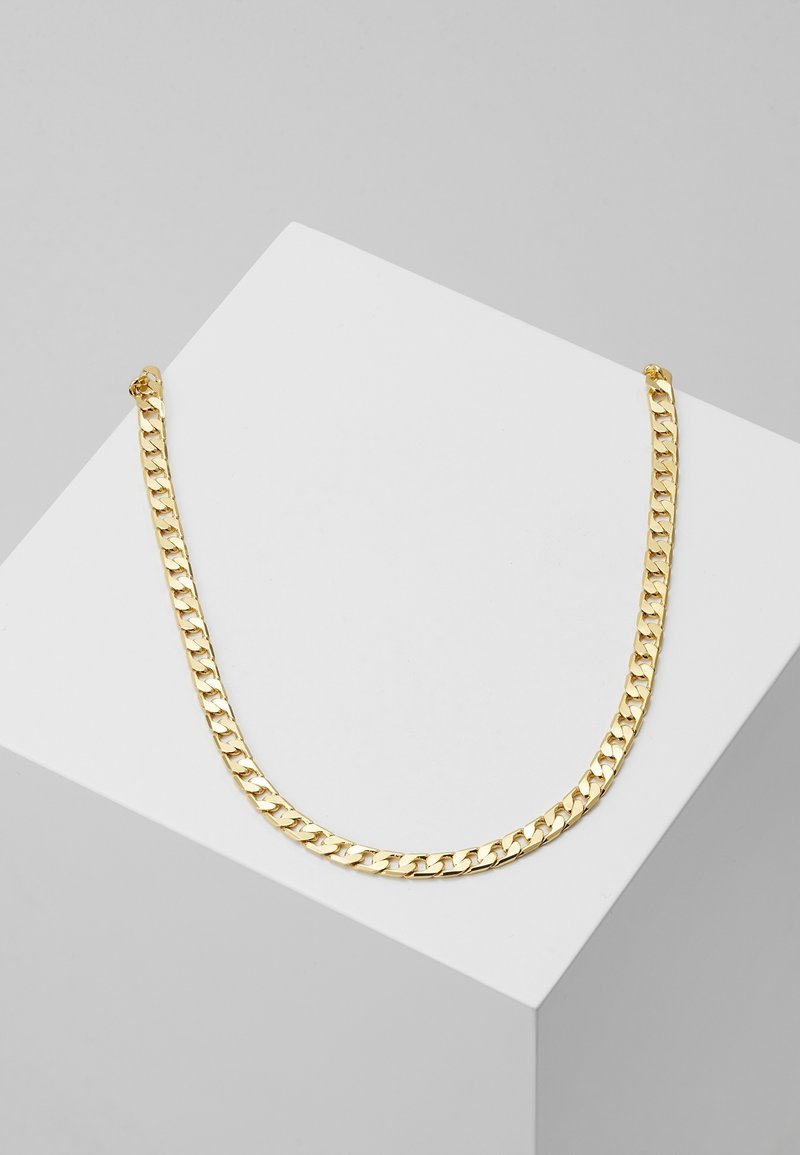 Collier chaîne de couleur dorée avec des maillons épais entrelacés exposé sur une surface blanche inclinée sur un fond gris.