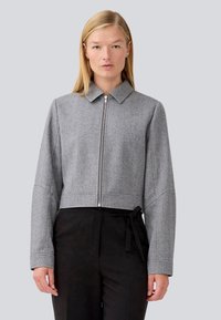 Sivi herringbone skraćeni sako s kragnom, prednjim zatvaračem i dugim rukavima. Uparen s crnim hlačama visokog struka s detaljem vezivanja.