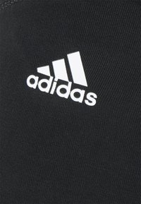 Te fabric preto atlético com um logotipo branco da Adidas. O material é suave com um acabamento texturizado, projetado para desempenho e conforto.