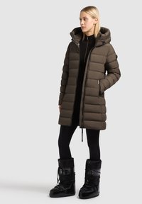 Polstret parka i mørke olivengrøn med hætte, lynlås foran og sidelommer. Sammen med sorte snesko med snørebånd og en struktureret overflade.