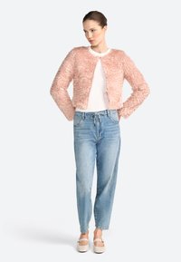 Giacca rosa fuzzy con scollo rotondo e maniche lunghe, abbinata a una maglietta bianca e jeans larghi azzurri chiari, completata da scarpe chiare.