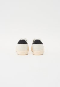 White and black suede sneakers with a minimalist design, featuring a textured upper, beige rubber sole, and subtle branding on the heel.