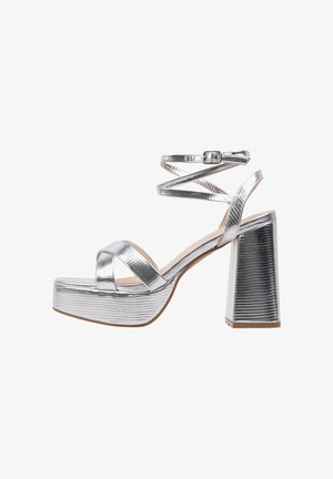 Sandales à plateforme argentées avec une finition métallique texturée, présentant des brides croisées à la cheville et un talon épais.