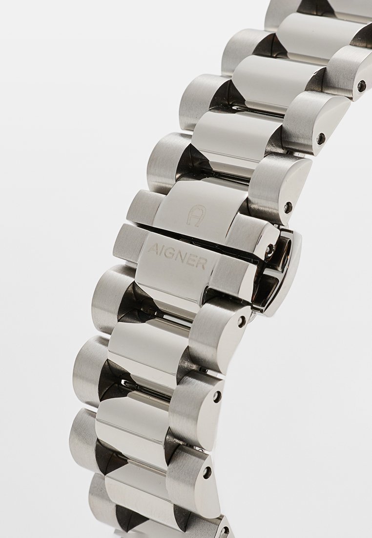 Silberner Edelstahl-Uhrenarmband mit abgerundeten Gliedern, das eine gebürstete Oberfläche und ein graviertes Logodetail aufweist. Verstellbares Verschlusssystem.