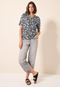 Camisa de manga corta en patrón abstracto en blanco y negro, combinada con jeans de pierna ancha de color gris claro y sandalias negras con acentos de hardware dorado.