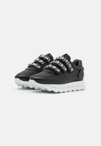 Svarta lädersneakers med tre reflektiva remmar, vit mellansula och texturerad genomskinlig yttersula. Har en elegant, modern design.