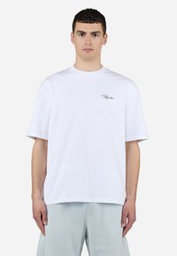 Camiseta de algodón blanca con un corte relajado. Presenta un pequeño logotipo en escritura negra en el lado izquierdo del pecho. Mangas cortas y cuello redondo.