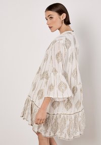 Weißes Kleid mit goldfarbener Blumenstickerei, Glockenärmeln, schichtsaum und lockerer Passform, das aus einem strukturierten, leichten Stoff besteht.
