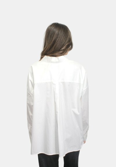 Camicia bianca a maniche lunghe vista dal retro, con colletto semplice, polsini regolabili e taglio dritto senza motivi visibili.