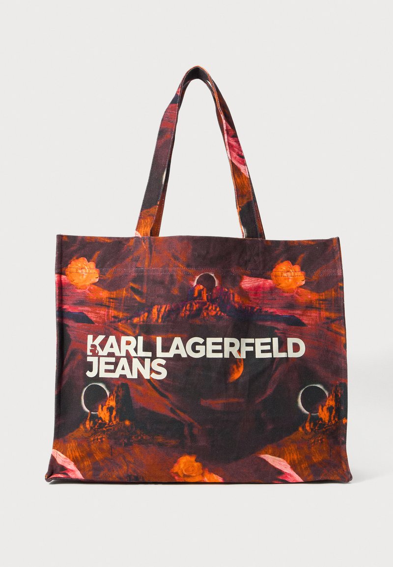 Tote bag med mørkerød og oransje abstrakt landskapsprint, med hvit tekst "KARL LAGERFELD JEANS" og to stoffhåndtak.