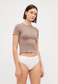 Short-sleeve, fitted top in taupe fabric with a smooth texture and crew neckline, paired with white high-waisted briefs.