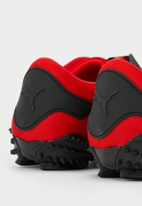 Røde og svarte joggesko med mesh-overdel, gummidetaljer og strukturert yttersåle med fremtredende pigger for godt grep.