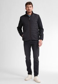 Giacca a vento imbottita con parte anteriore trapuntata in nero, dotata di colletto alto, chiusura con zip e polsini elasticizzati. Abbinata a jeans scuri e sneaker.