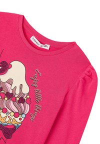 Różowa bawełniana koszula z długim rękawem z grafiką babeczki ozdobioną brokatem oraz napisem "Ciesz się małymi rzeczami." Okrągły dekolt i bufiaste rękawy.