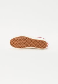Sneaker sole in beige with a diamond pattern, featuring a solid red accent at the heel and textured grip for traction.