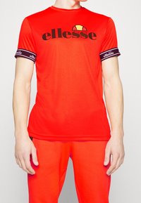 Rød atletisk T-shirt med korte ærmer, prydet med et sort logo og lila kantede ærmer. Fremstillet af glat stof, har den en klassisk pasform.