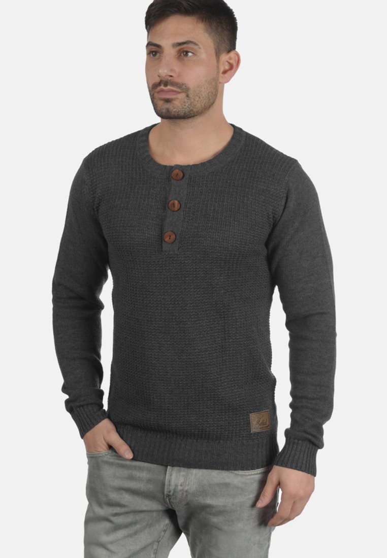 Maglione lavorato a maglia grigio scuro con scollatura a girocollo, tre bottoni in legno, polsini a costine e una piccola etichetta in pelle del marchio sull'orlo.