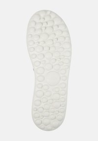 Valkoiset kenkien pohjat, joissa on karhennettu pinta, jossa on erilaisia kohoavia ympyräkuvioita. Pohjassa on brändin nimi "Camper".