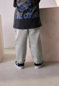 T-shirt graphique noir avec un design cosmique ; pantalon en denim délavé, coupe décontractée ; baskets noires avec semelles blanches et accents de logo.