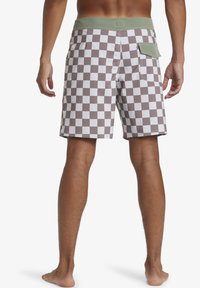 Men's swim shorts in a brown and white checkerboard pattern. Features a green elastic waistband and a back pocket with a flap.