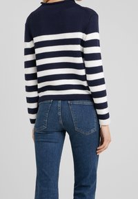 Navy- und weiß gestreifter Strickpullover mit schütterem Kragen und langen Ärmeln, kombiniert mit enganliegenden, dunkelblauen Jeans mit Gesäßtaschen.