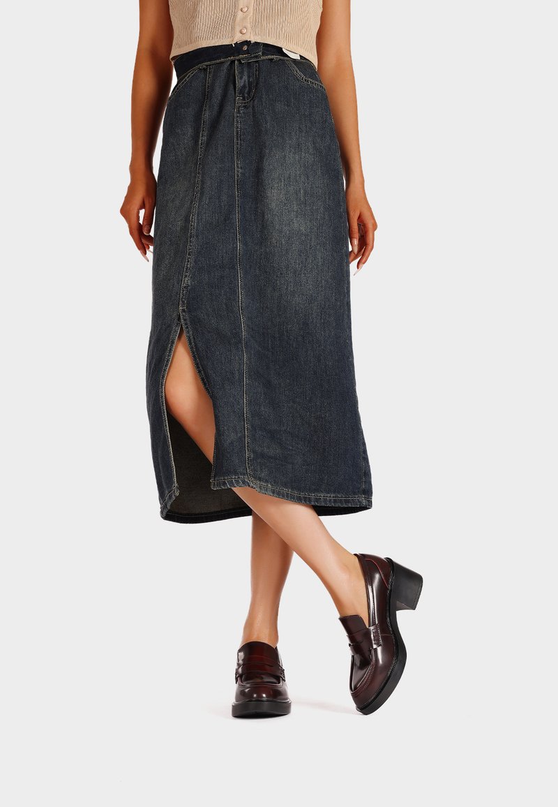 Gonna midi in denim scuro con uno spacco frontale, caratterizzata da un'alta vita e passanti per cintura. Indossata con mocassini chunky con tacco marroni.