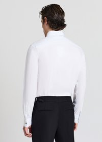 Camicia bianca a maniche lunghe, polsini con bottoni e colletto classico. La parte posteriore mostra una texture liscia e una vestibilità sagomata, abbinata a pantaloni neri.