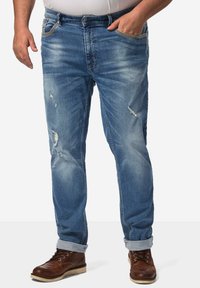 Jeans de mezclilla azul claro con un corte relajado, que presentan un diseño desgastado y los dobladillos enrollados. Se llevan con botas marrones de cordones.