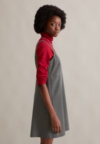 Grau gestreiftes Kleid, das über einem roten Rollkragenpullover getragen wird. Das Kleid hat eine ausgestellte Silhouette und dünne Träger. Die kurzen Ärmel des Rollkragenpullovers sind sichtbar.