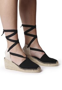 Espadrillas nere in tela con tacco in juta intrecciata, featuring fascette incrociate nere attorno alle caviglie e un retro beige testurizzato.