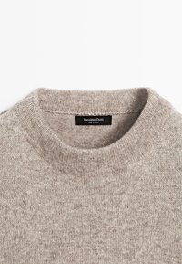 Béžový pletený svetr s kulatým výstřihem, vyrobený z texturované tkaniny. Na etiketě je napsáno "Massimo Dutti." Žádné viditelné vzory nebo akcenty.