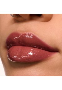 Glanzende lipkleur in een roze-bruin tint met fijne glitters. De lippen lijken vol en glad, met een lichte glans en een natuurlijke textuur.