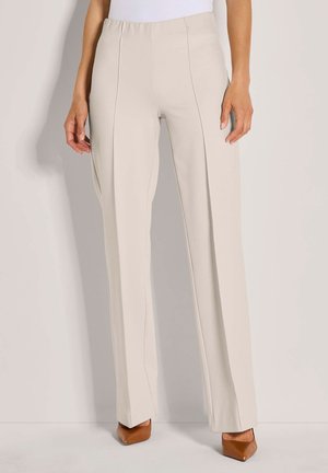 Beige hoge taille rechte broek gedragen met een witte top en bruine puntige hakken, staande tegen een effen achtergrond.