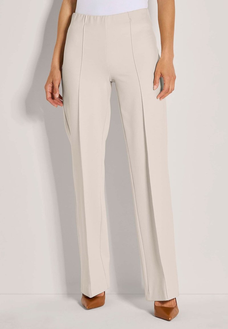 Beige hoge taille rechte broek gedragen met een witte top en bruine puntige hakken, staande tegen een effen achtergrond.