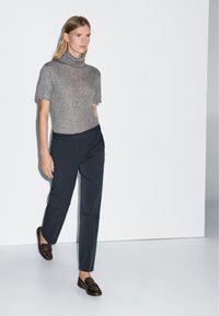 Grijze coltrui, op maat gemaakte donkere broeken en bruine instappers. Eenvoudig, strakke ontwerp met een gladde textuur en neutraal kleurenpalet.