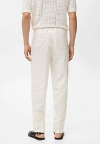 White linen trousers with a tailored fit, featuring two back pockets and a mid-rise waistband. Worn with a loose, knitted top and black sandals.