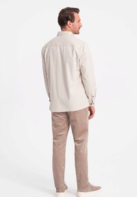 Lichtbeige geknopte shirt met een rugpas, lange mouwen en manchetten. Gepaard met bruin corduroybroeken en lichtgekleurde sneakers.