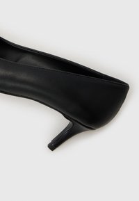 Sorte lær høye hæler med et elegant design, spiss tå og smal hæl. Teksturen er glatt med søm langs kantene.