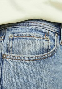 Denim jeans in een lichte blauwe kleur, standaard achterzakdetails, zichtbare stiksels en metalen klinknagels die de randen van de zakken accentueren.