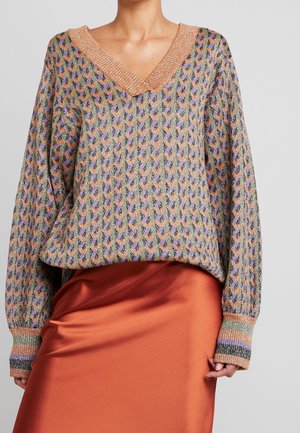 Femme portant un pull en maille multicolore avec un col en V et une jupe en satin orange.