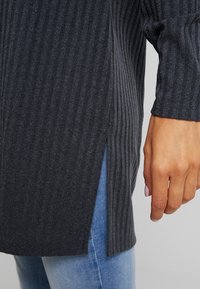 Mörkgrå ribbade tröja med sidodel, långa ärmar och en texturerad tyg. Kombination med ljusblå denimjeans.