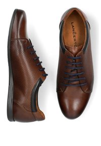 Brązowe skórzane buty z perforowanym wzorem, granatowymi sznurowadłami i gładkimi akcentami. Posiadają czarną gumową podeszwę i okrągły czubek.