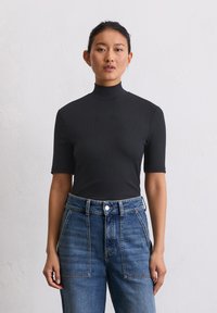 Zwarte geribde top met korte mouwen en hoge hals, gecombineerd met high-waisted blauwe denim jeans met dubbele voorkruiden.