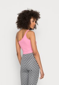 Top cropped de algodão, ajustado, em rosa com alças finas. Combinado com leggings de cintura alta em padrão xadrez preto e branco, apresentando uma textura elástica.