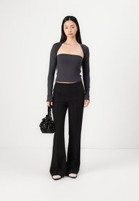 Black flared trousers paired with a dark gray long-sleeve top. The model holds a small black bag with floral accents. Indoor setting.