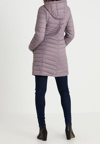 Lyslilla puffjakke med hætte, der har vandret syninger, en tætsiddende silhuet og som bæres med mørke jeans og ankelstøvler.