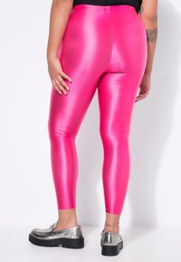 Huomiota herättävät fuksia leggingsit kiiltävästä, joustavasta materiaalista, jossa on korkea vyötärö, sileä pinta ja tiukka istuvuus, yhdistettynä hopeanvärisiin metallisiin kenkiin.