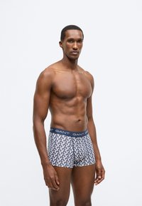 Boxershorts mit einem marineblauen Bund mit "GANT"-Logo und einem weißen, wiederholten Muster auf blauem Hintergrund, gefertigt aus einem weichen Stoff.