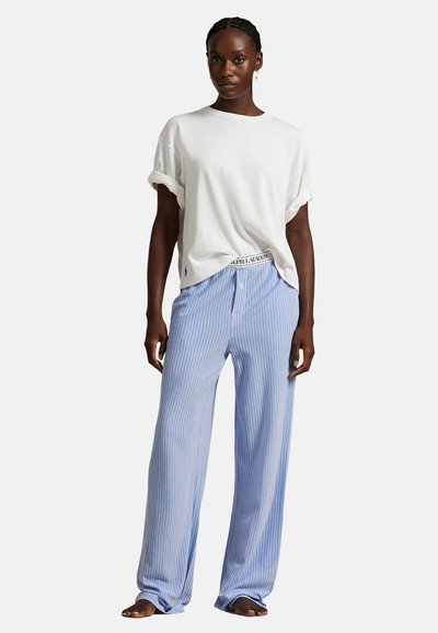 Witte oversized t-shirt met opgerolde mouwen, gecombineerd met lichtblauwe gestreepte pyjamabroek met een elastische tailleband en een knoopsluiting aan de voorkant.