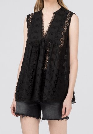 Blusa senza maniche in pizzo nero con motivi floreali abbinata a shorts di denim neri sfrangiati su una persona in piedi davanti a uno sfondo semplice.